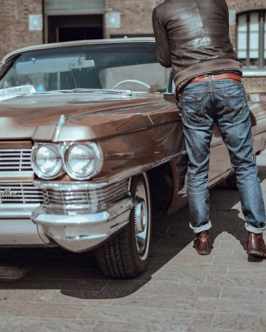 man in blue denim pants standing beside brown car