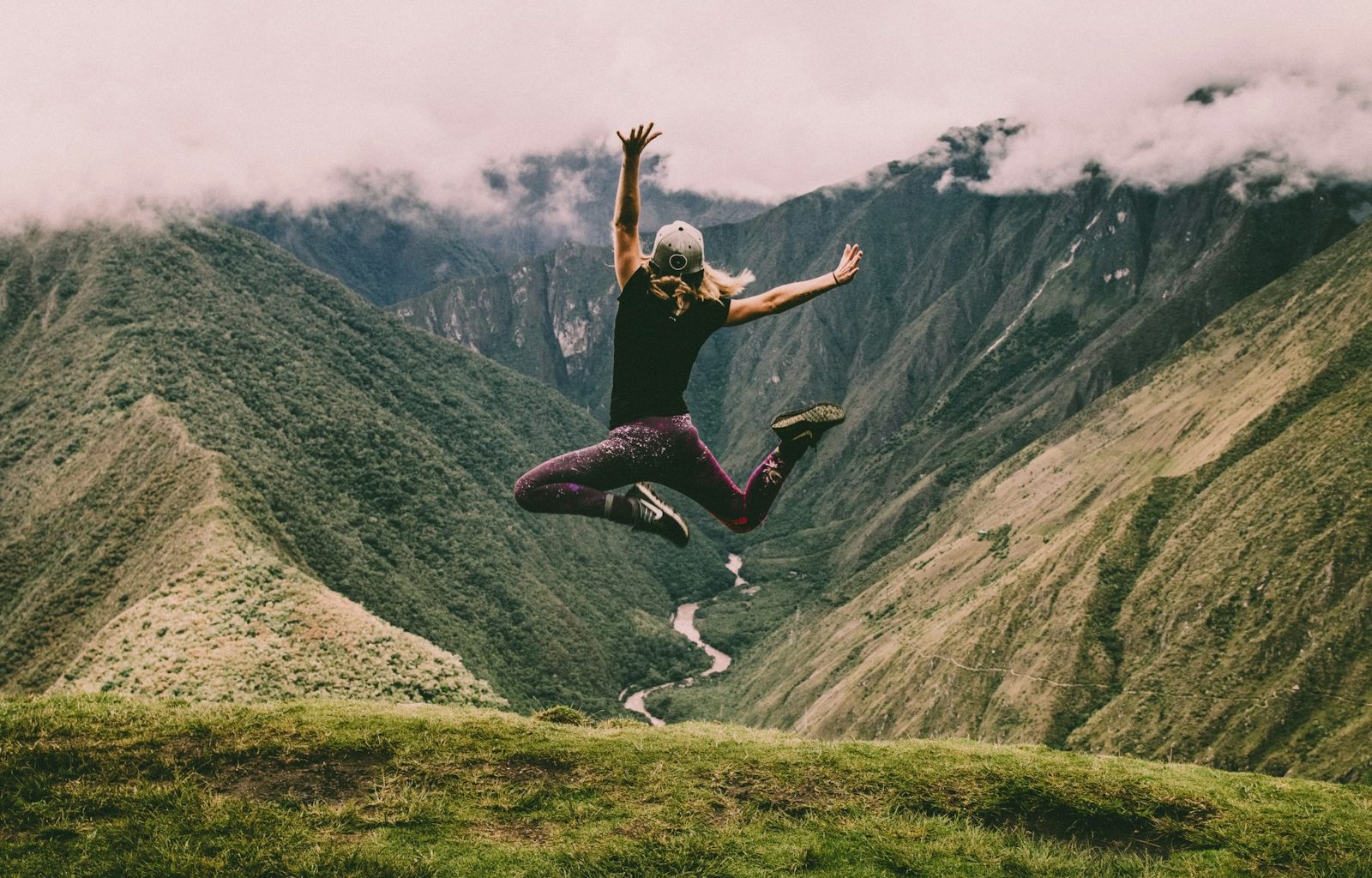 woman jumping on green mountains