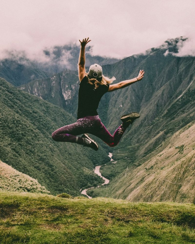 woman jumping on green mountains