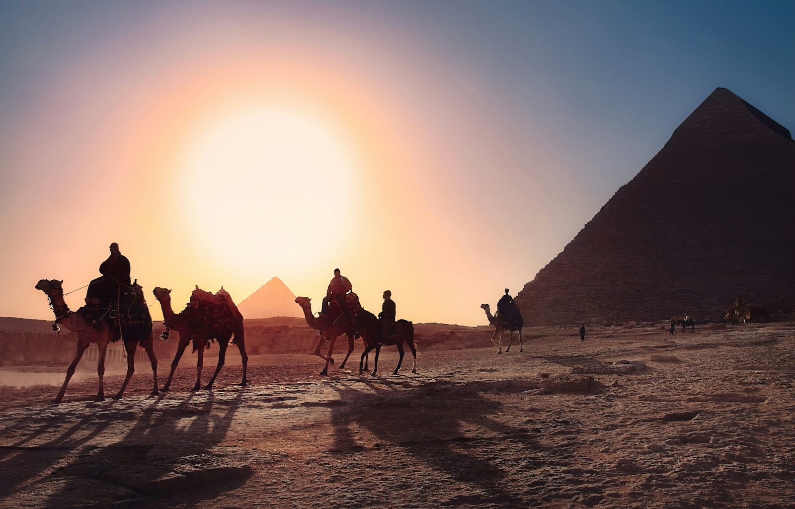 five persons riding camels walking on sand beside Pyramid of Egypt