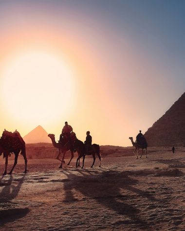 five persons riding camels walking on sand beside Pyramid of Egypt