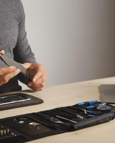 Iemand repareert een smartphone met een schroevendraaierset en plastic gereedschap op een werkblad